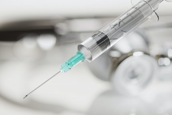 Disposable syringe for vaccine injection on gray background.