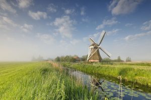 windmill on green meadow by river