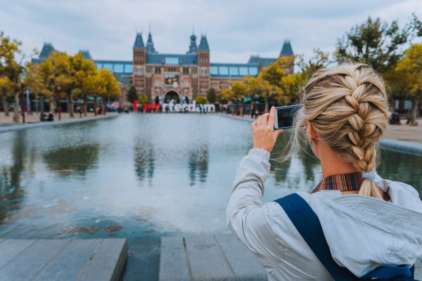 Woman tourist taking photo of the Rijksmuseum in Amsterdam on the mobile phone. Travel in Europe