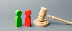 Wooden figures of people standing near the judge's gavel. Litigation. Business rivals. Conflict of interest. Law and justice. The layer's services. Two opponents. Judgment. Gavel. Red and green