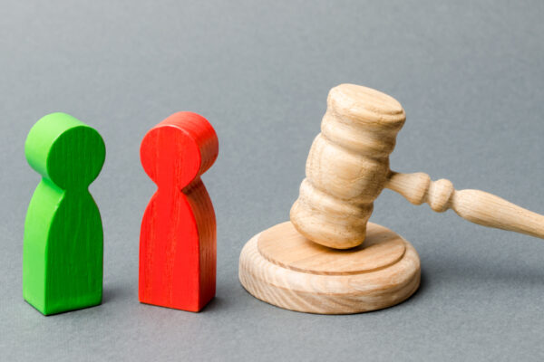 Wooden figures of people standing near the judge's gavel. Litigation. Business rivals. Conflict of interest. Law and justice. The layer's services. Two opponents. Judgment. Gavel. Red and green